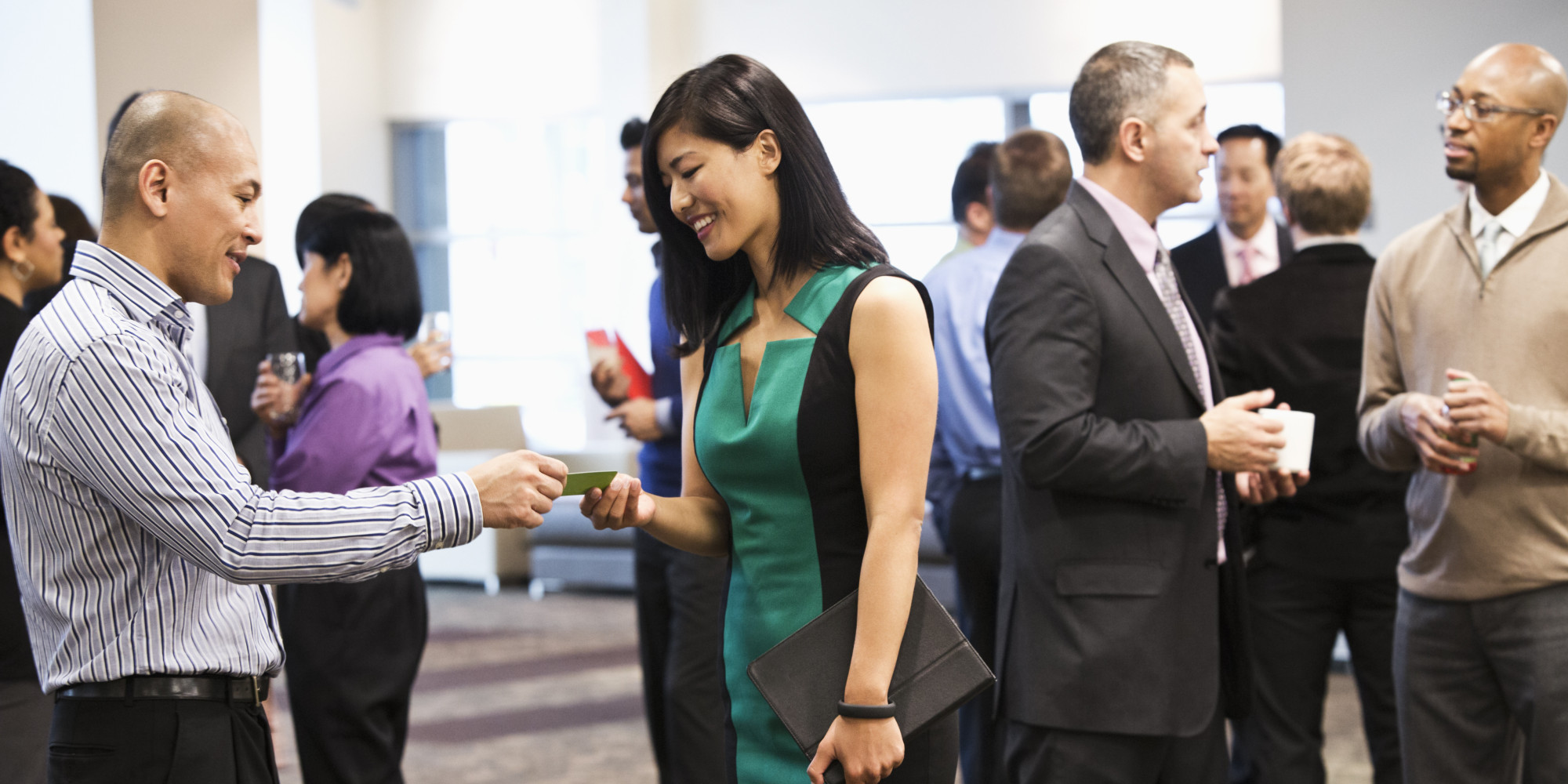 A man and woman exchanging business cards at a crowded networking opportunity at an event like our Learn EB-5 Seminar.