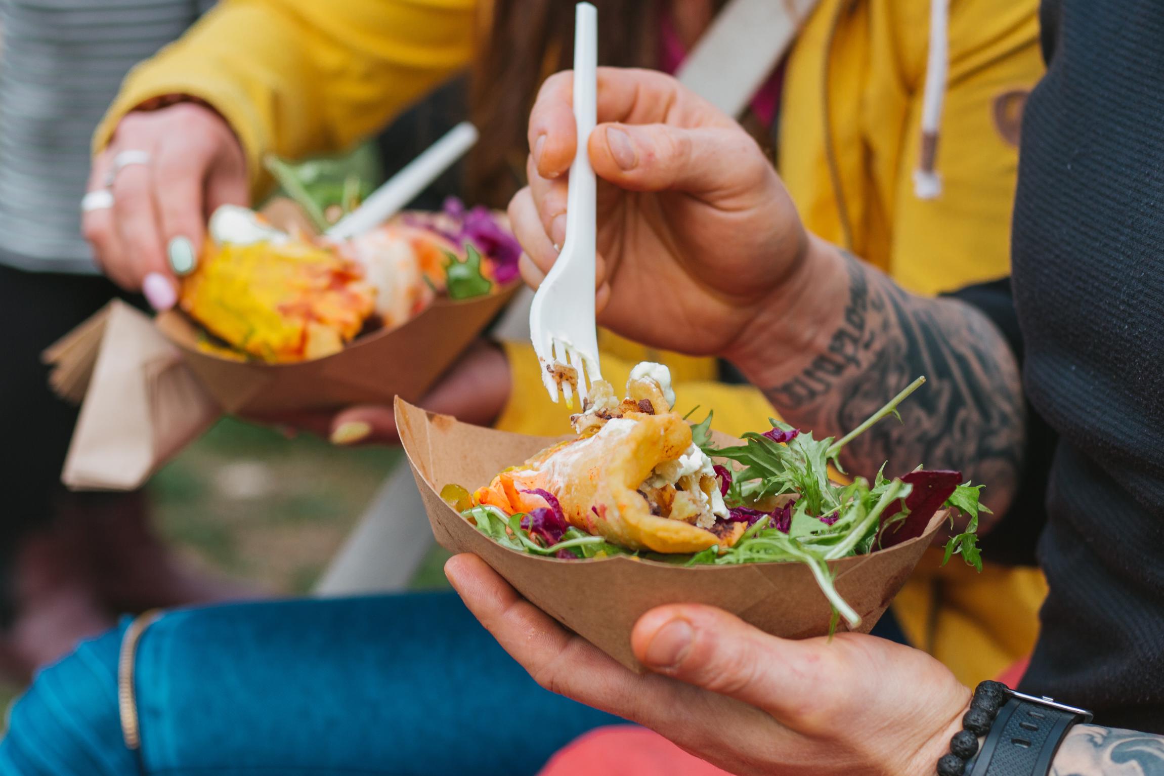 HANDS HOLDING FORKS IN PAPER BOAST FULL OF VEGAN TACOS AND SALAD. AT VEGFEST.