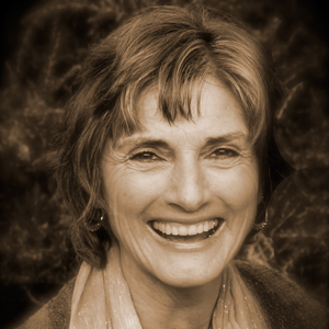 a short and brown haired woman grins happily at the viewer. she has highlights in her hair and appears to be wearing a light colored scarf around her neck. she has small round earrings on. her eyes are brown. this is a sepia toned image.