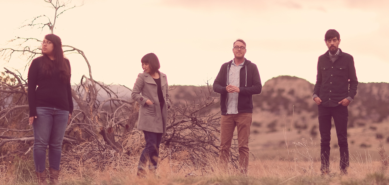 the band haunted windchimes stands in a dessert background. there are four individuals standing in a line