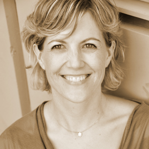 a portrait of a woman with blond hair at about chin length with side swiped bangs and happy eyes smiles at the viewer. she is wearing a scoop-necked top and a small silver necklace. the photo has a sepia tone.