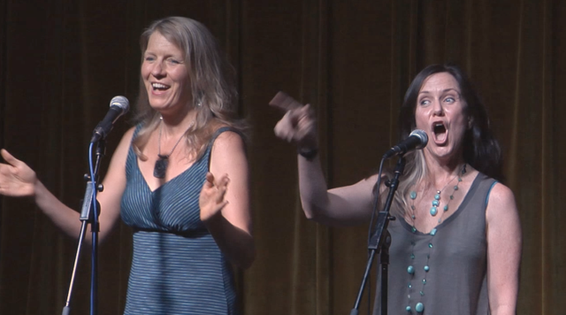 image of two women, Nina Rolle & Johanna Walker, performing on stage at microphones