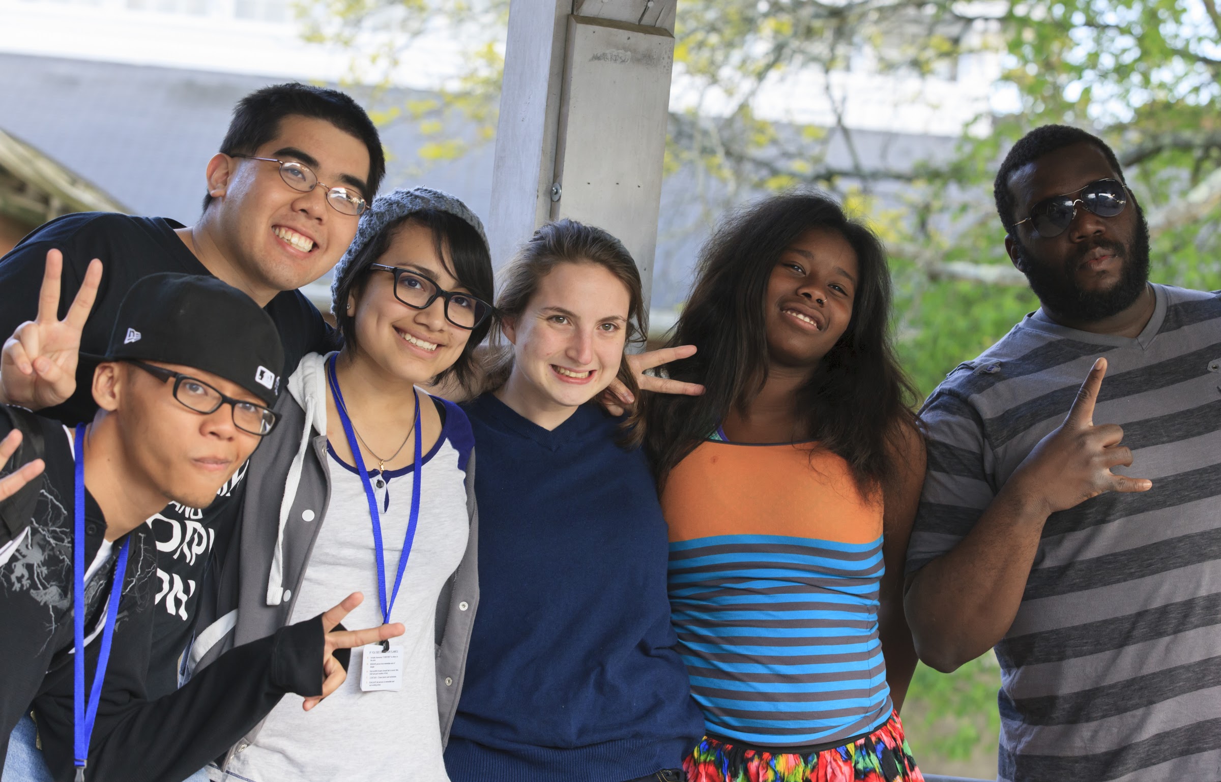 Six young people facing forward, arms interlinked, smiling and giving peace signs