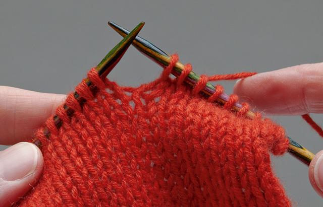 Picture of hands knitting with reddish orange yarn.